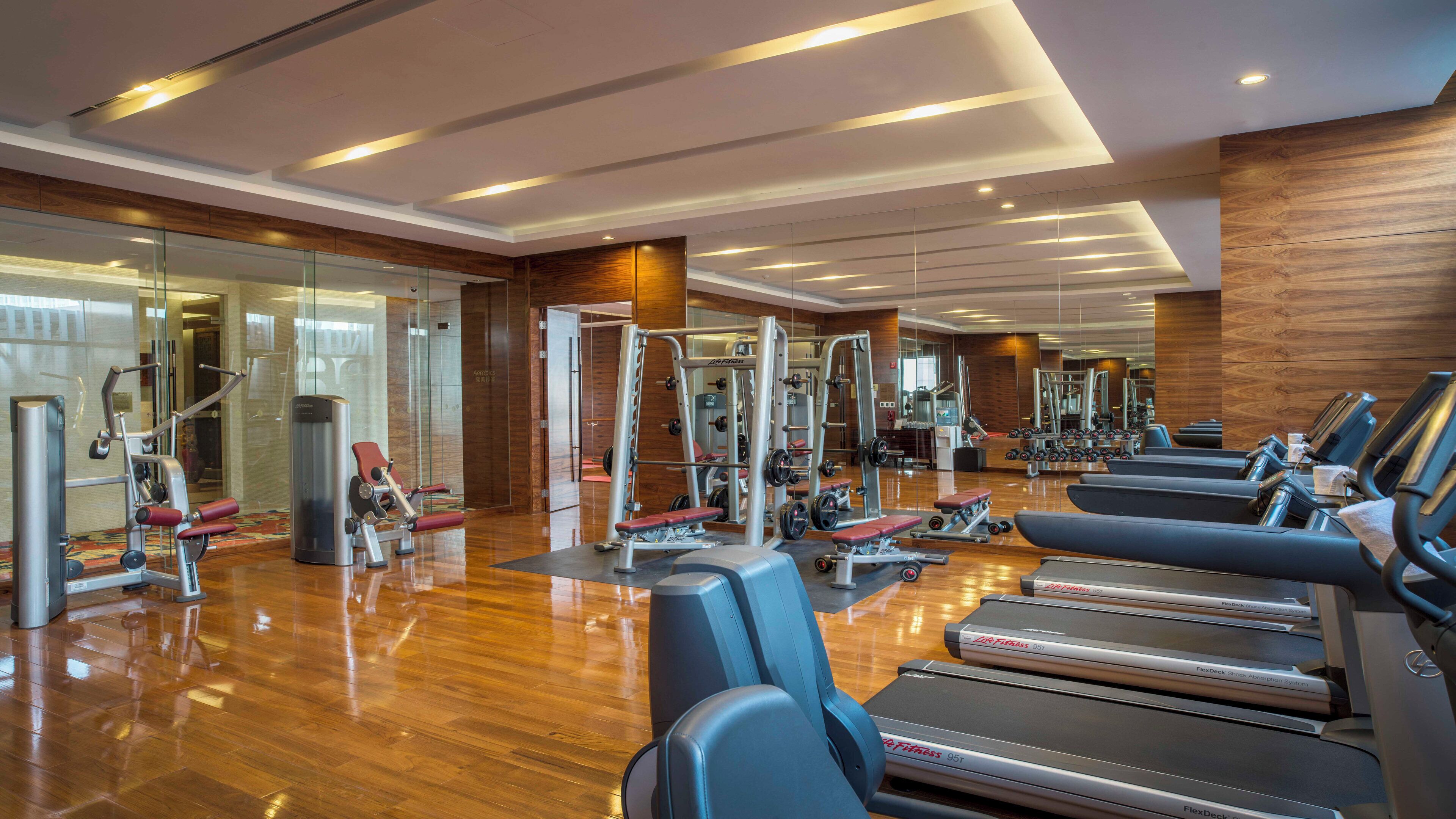 Una sala de gimnàstica moderna equipada amb aparells cardiovasculars, màquines de peses i un terra de fusta.