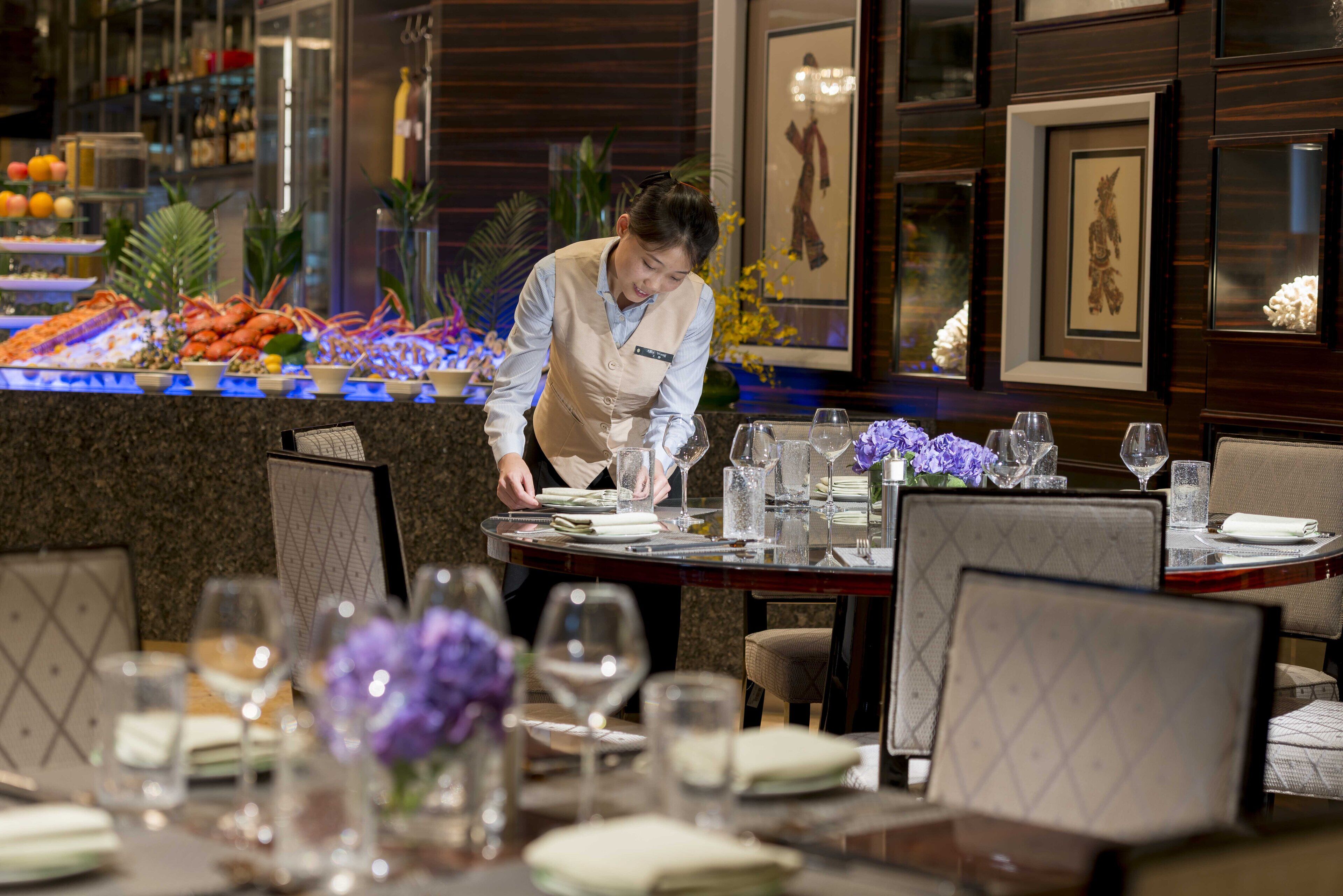 A well-set dining table with a server attending to it, surrounded by chairs and a decorative centerpiece.