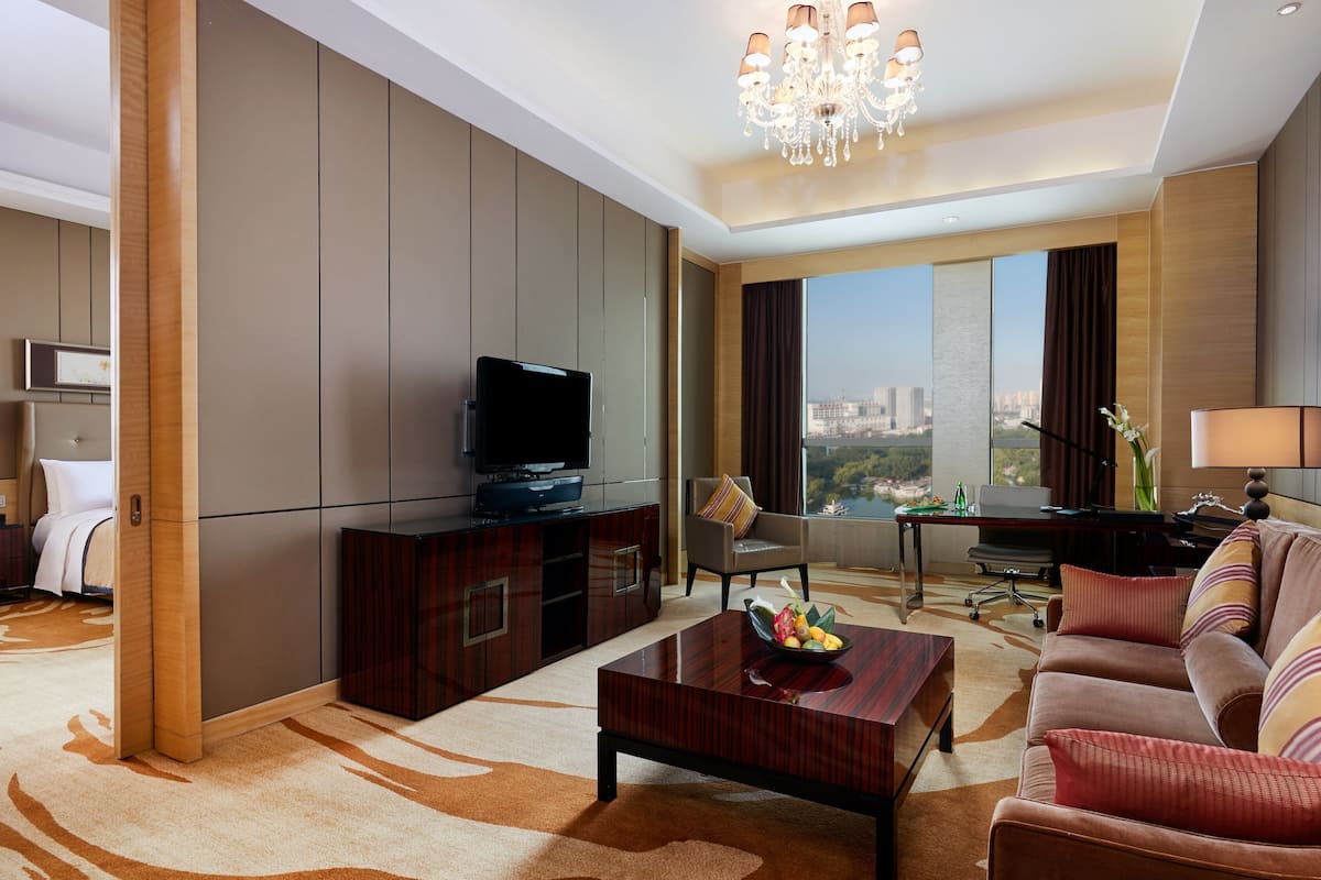A modern hotel room with a large bed, a TV, a desk, a sofa, and a view of the city.