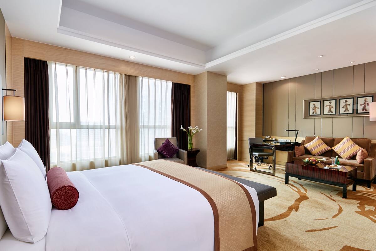 A hotel room with a large bed, a desk, a sofa, and a view of the city.