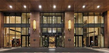 A hotel entrance with a glass facade, a traditional Asian-style gate, and a well-lit interior.