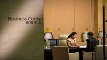 A business center with a sign, a desk with a computer, a lamp, and a vase with flowers.