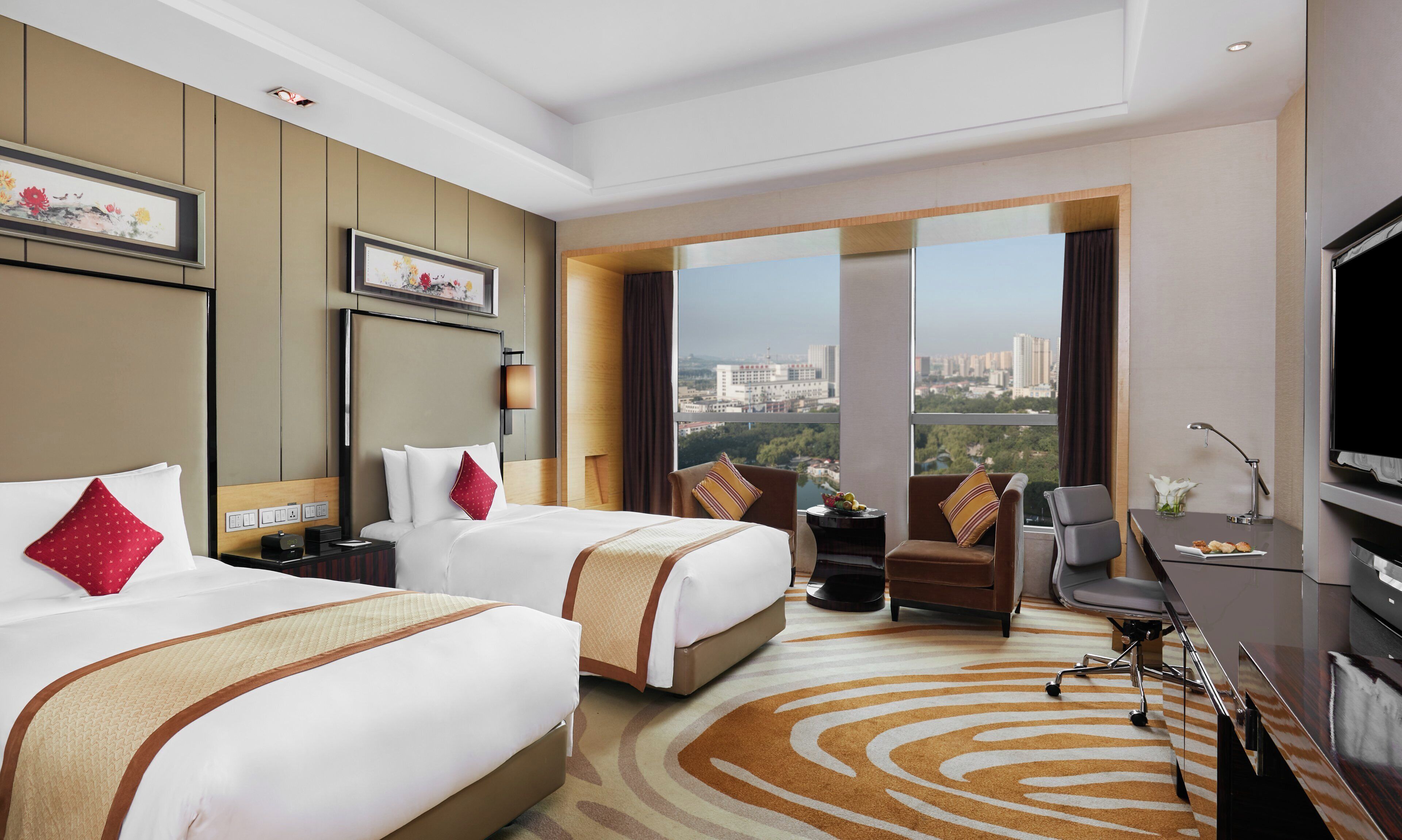 Habitación de hotel con dos camas, un escritorio, una silla, un televisor y un ventanal con vistas a la ciudad.