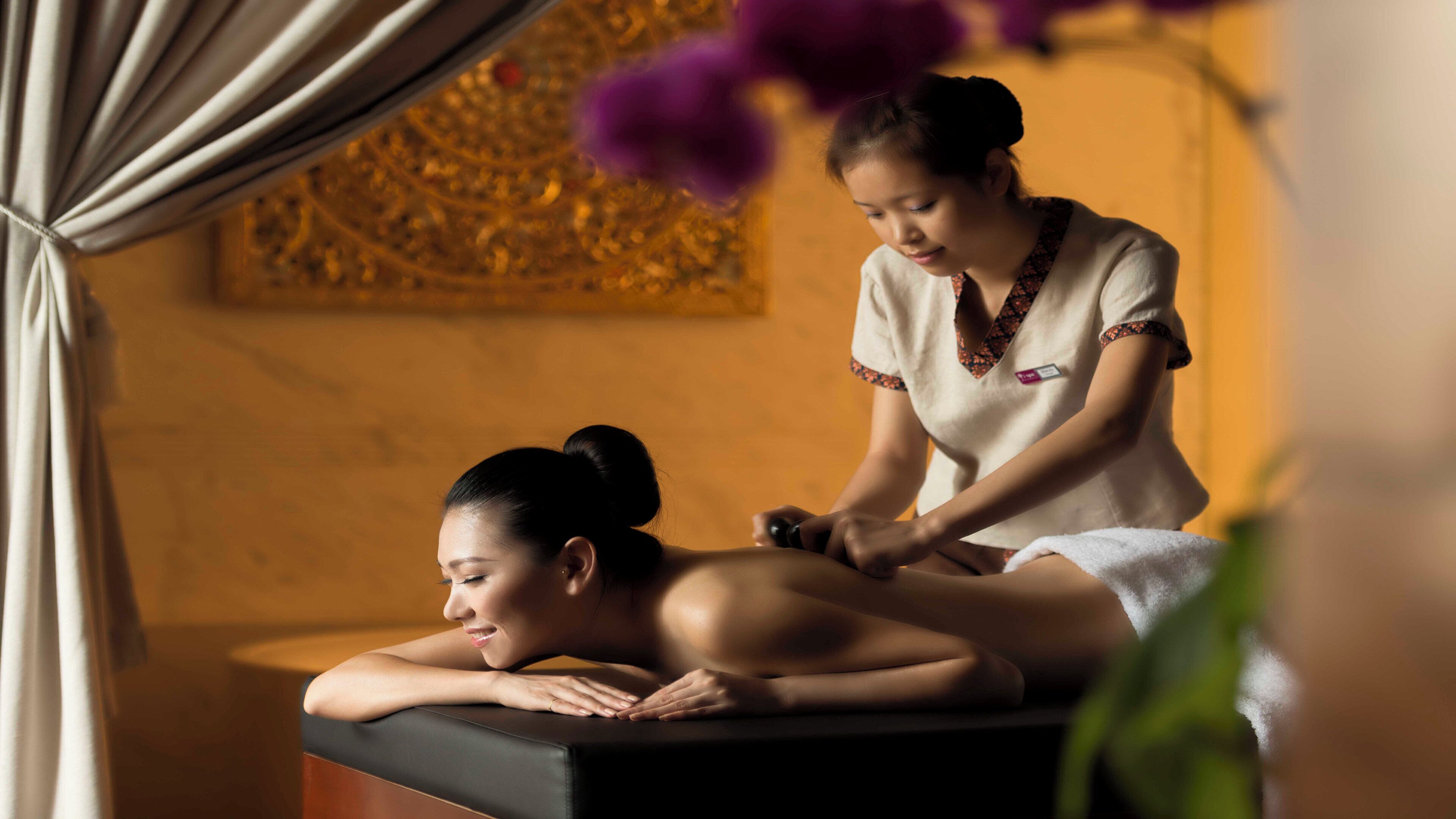 A massage therapy session in a room with a massage table, a curtain, and a decorative wall.
