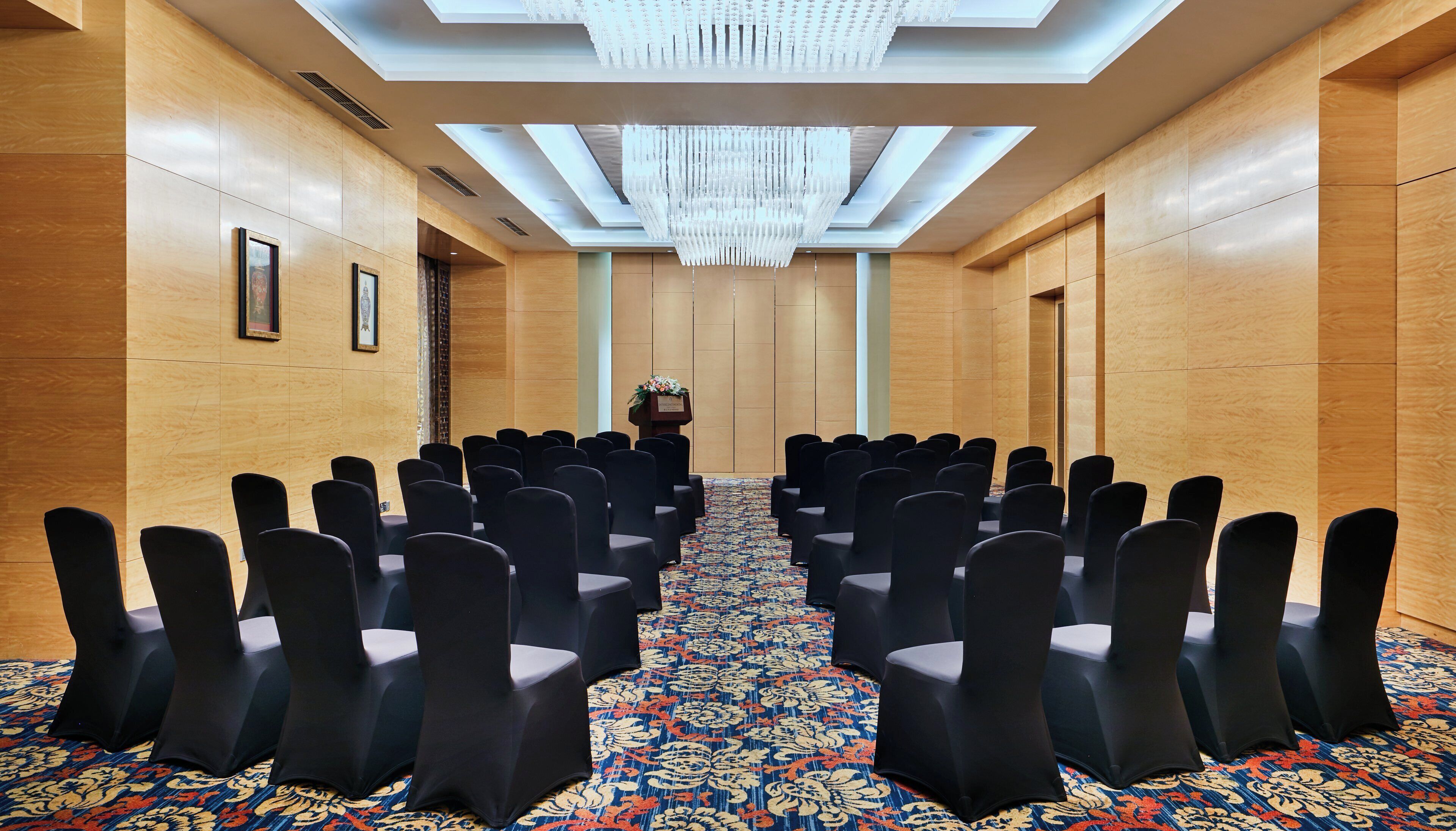 A conference room with rows of chairs, a podium, and a chandelier.