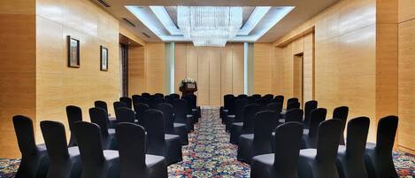 A conference room with rows of chairs, a podium, and a chandelier.