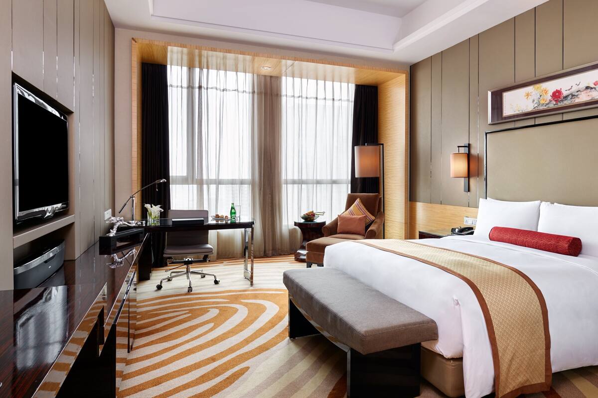 A hotel room with a large bed, a desk with a chair, a television, and a window with curtains.