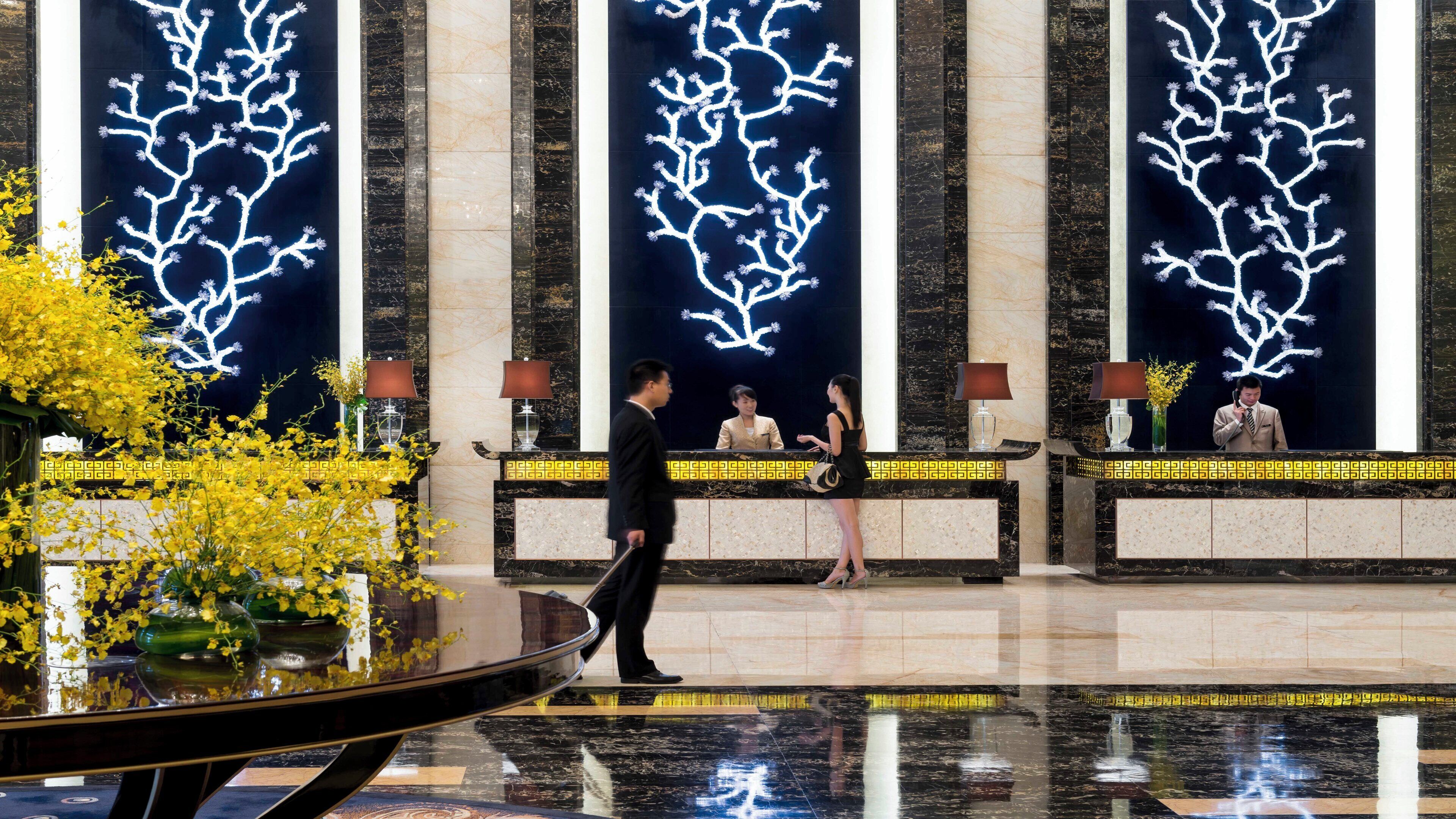 A hotel reception area with a modern design, featuring a marble reception desk, a digital tree display, and a reflection pool.