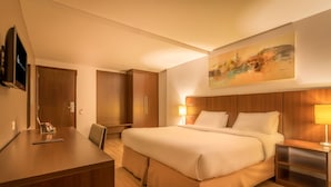 Ett hotellrum med en stor säng, ett skrivbord, en stol, en tv och en tavla på väggen.