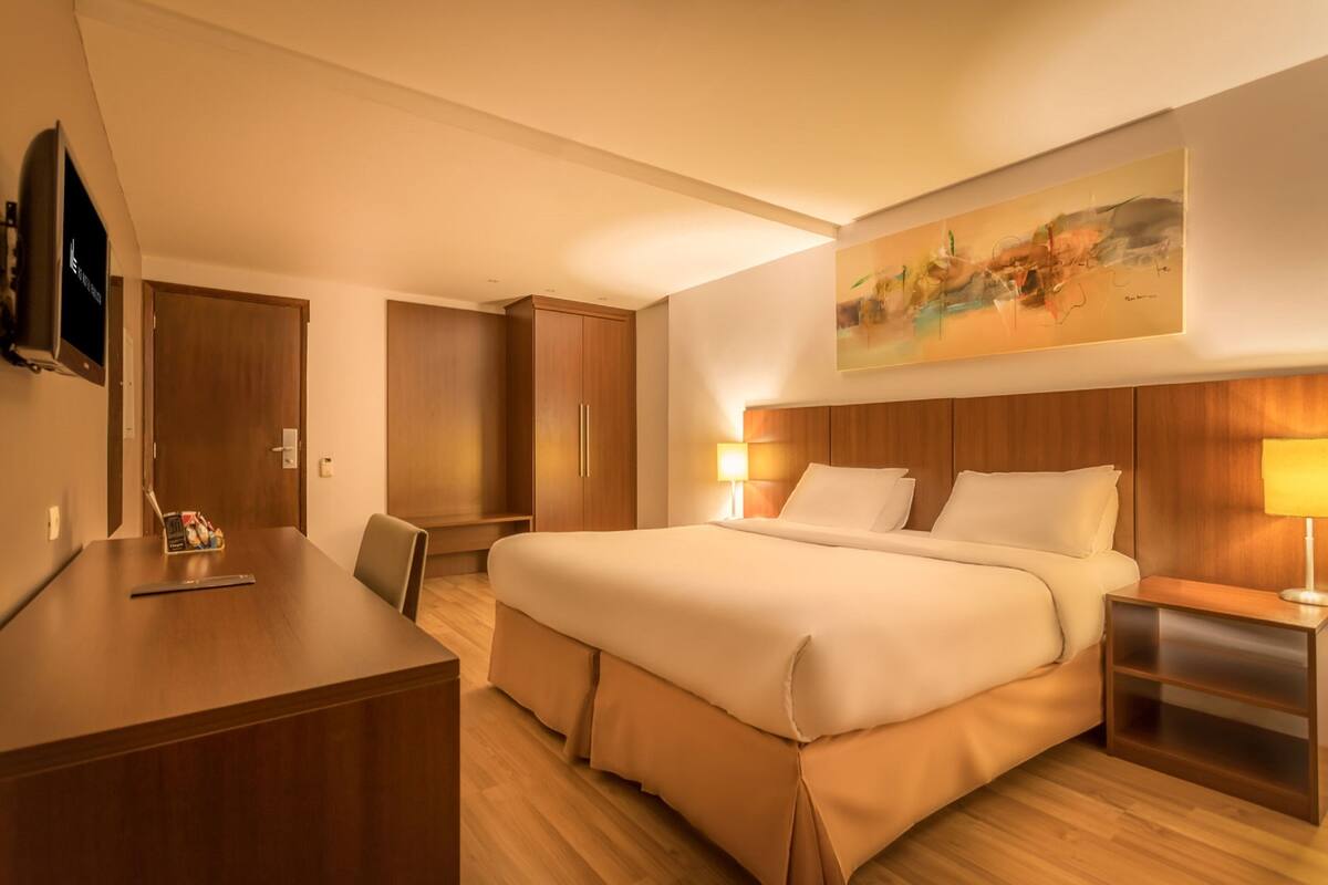 Une chambre d’hôtel avec un grand lit, un bureau, une chaise, une télévision et un tableau au mur.