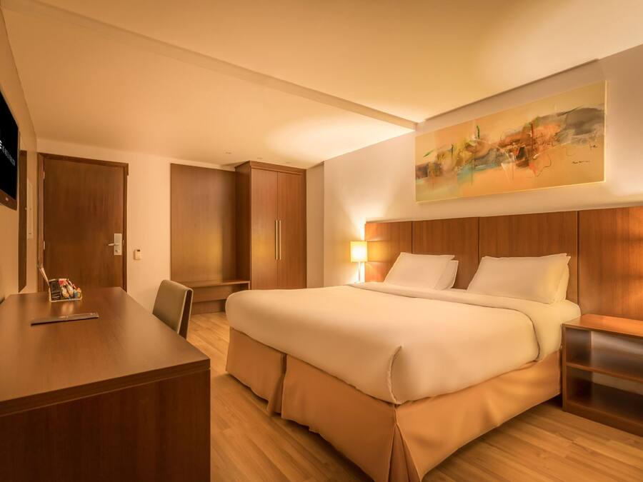 A hotel room with a large bed, a desk, a chair, a TV, and a painting on the wall.