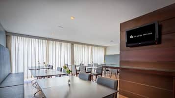Uma sala de conferências de hotel moderna, com televisão de tela plana na parede, painéis de madeira e uma grande janela com cortinas.