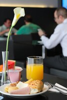 A breakfast setting with a plate of food, a glass of orange juice, a glass of milk, a slice of watermelon, and a calla lily.