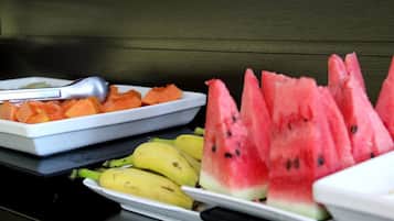Uma mesa de buffet com melancia fatiada, cenouras e bananas.