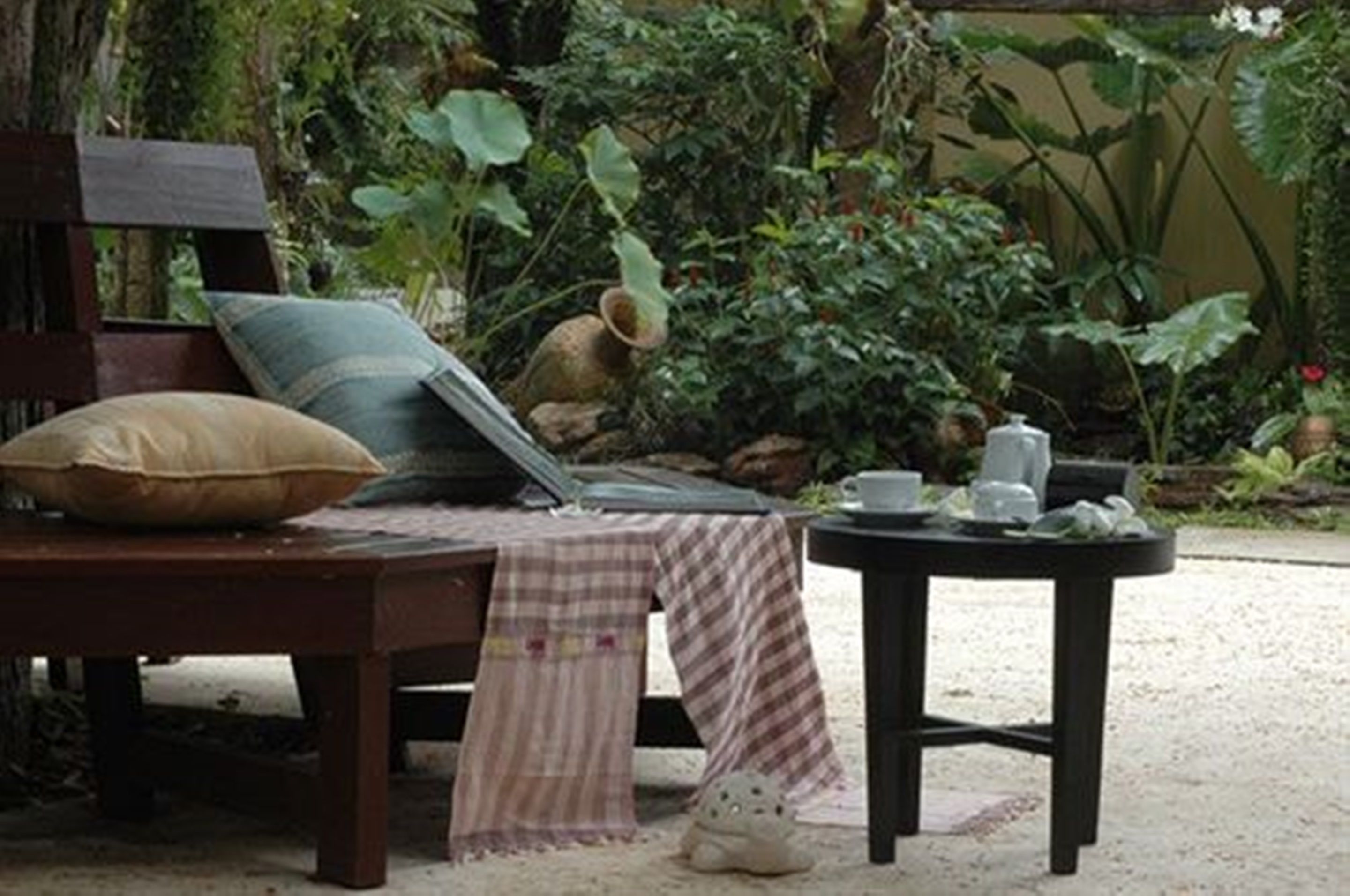 A wooden bench with a cushion and a table with a teapot and cups.