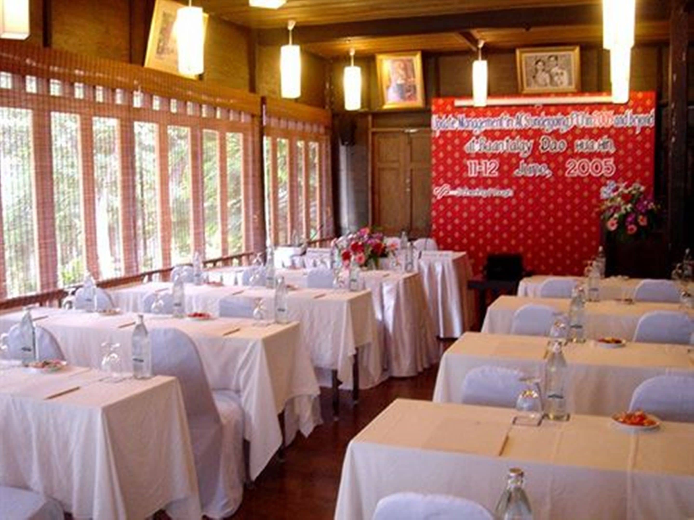 Een balzaal met gedekte tafels voor een formeel evenement, met een spandoek met tekst en een bloemstuk.