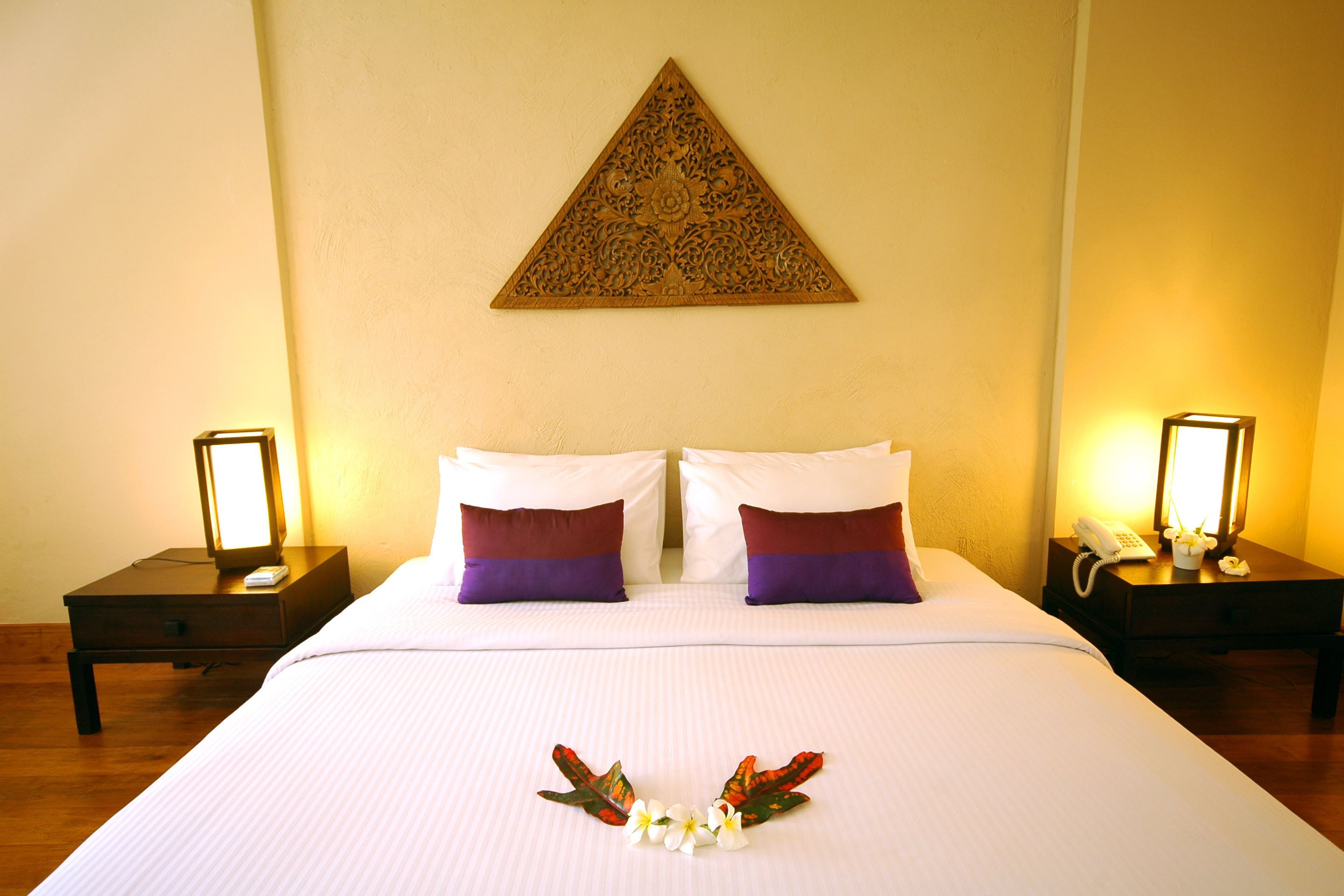 A hotel room with a neatly made bed, two bedside tables with lamps, and a decorative wall piece above the bed.