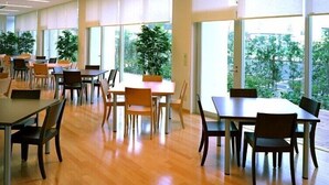 A spacious indoor area with multiple tables and chairs, large windows, and potted plants. - Hirata MAPLE Hotel (Izumo)