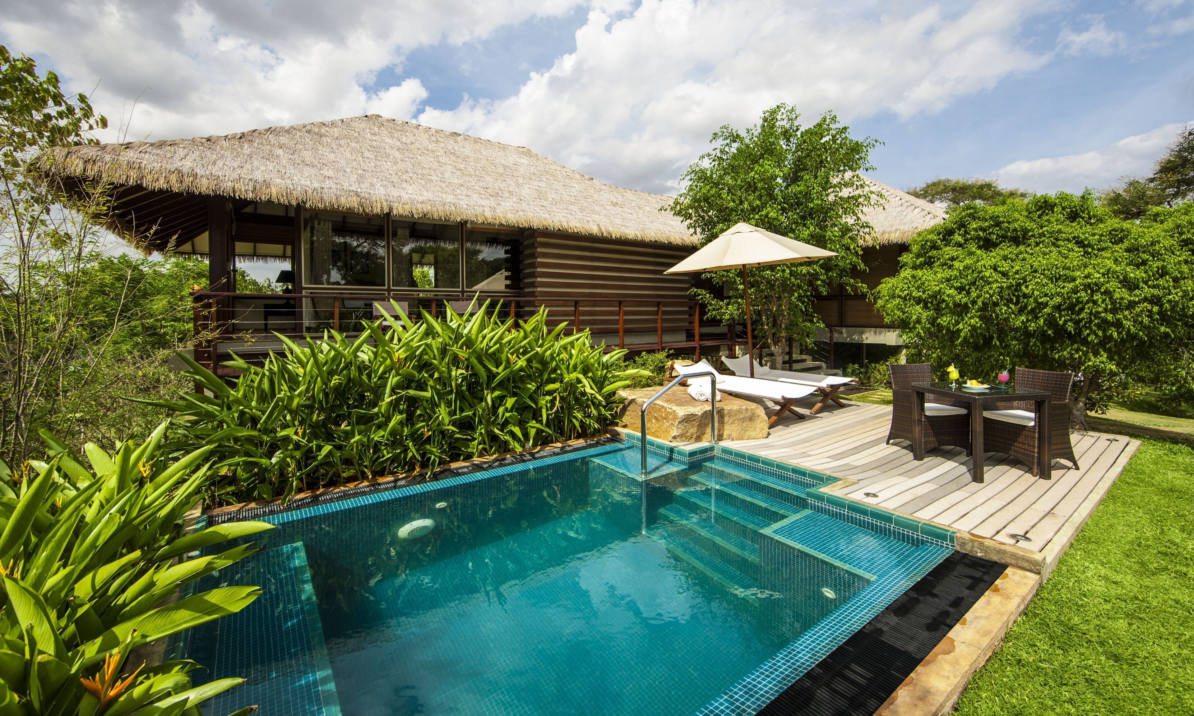 A poolside area with a thatched-roof structure, lounge chairs, and a wooden deck.