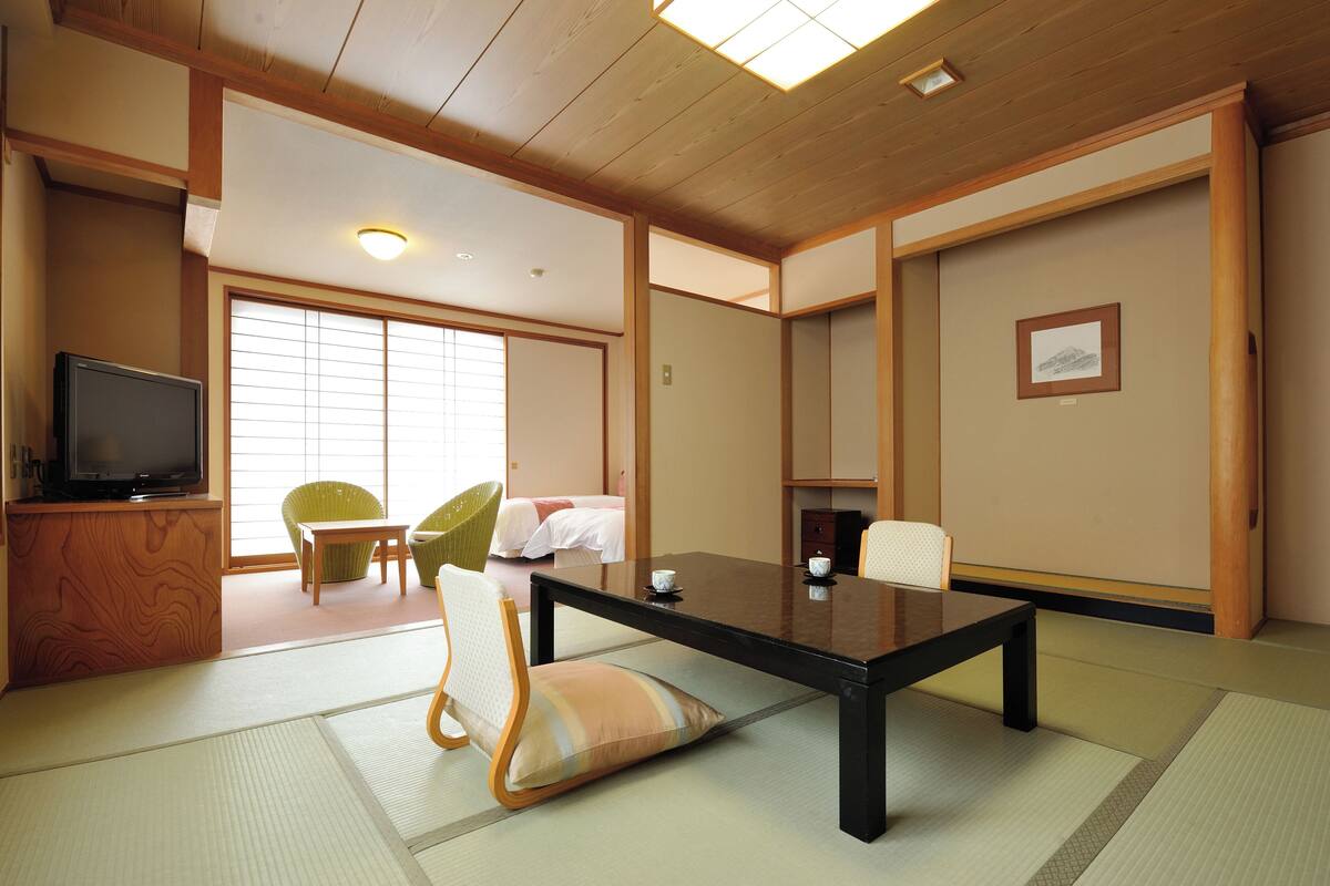 A traditional Japanese-style room with tatami flooring, a low table, and a television on a wooden stand.