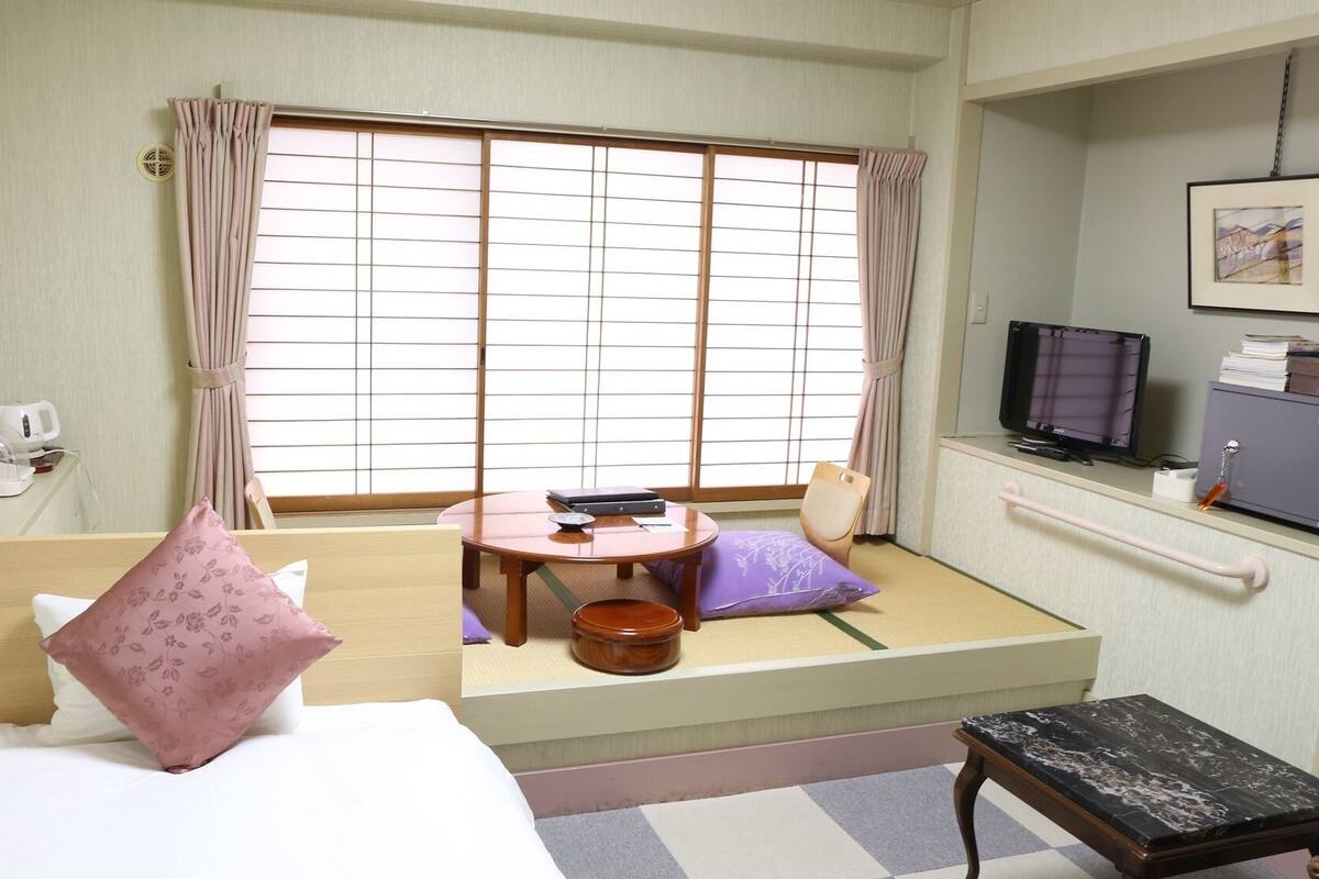 A room with a bed, a small table, a chair, a television, and a cabinet.