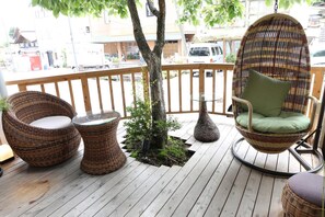 A wooden deck with wicker furniture, including two chairs and a small table, and a hanging chair with a cushion. - Uematsuya Ryokan (Ueda)
