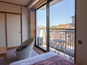 A hotel room with a large sliding glass door leading to a balcony with a view of a cityscape and mountains. - Uematsuya Ryokan (Ueda)