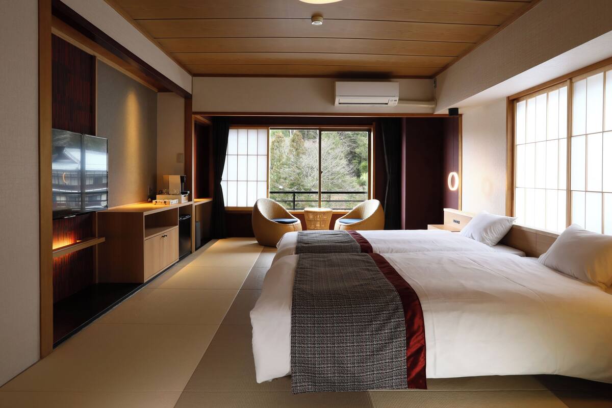 A modern hotel room with a large bed, a TV, a desk, and a balcony with a view of trees.
