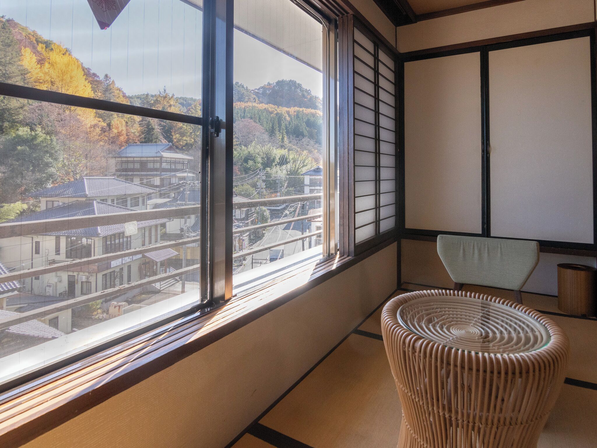Una habitación japonesa tradicional con suelo de tatami, una mesa de madera baja y vista a un edificio tradicional por una ventana grande.