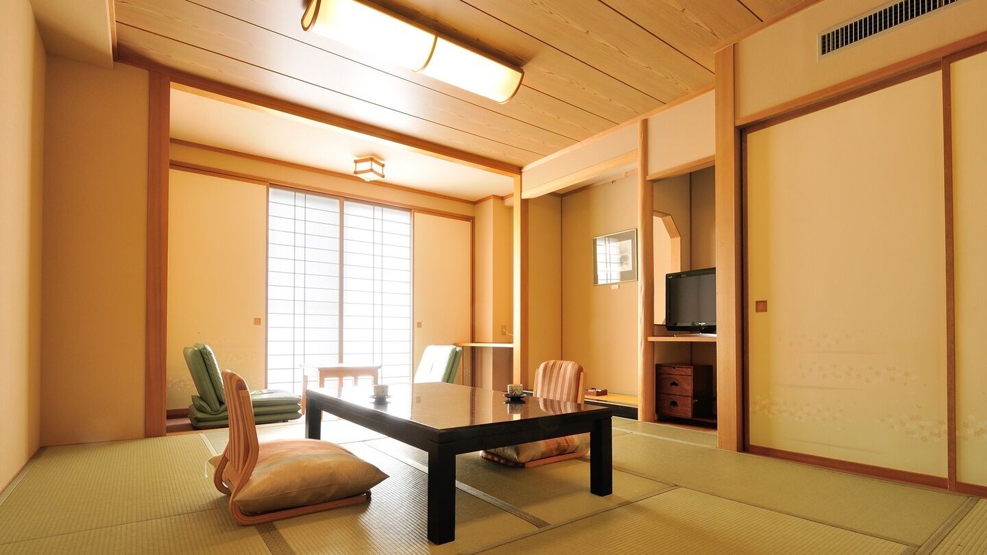 A traditional Japanese room with tatami flooring, a low table, chairs, a television, and sliding doors.