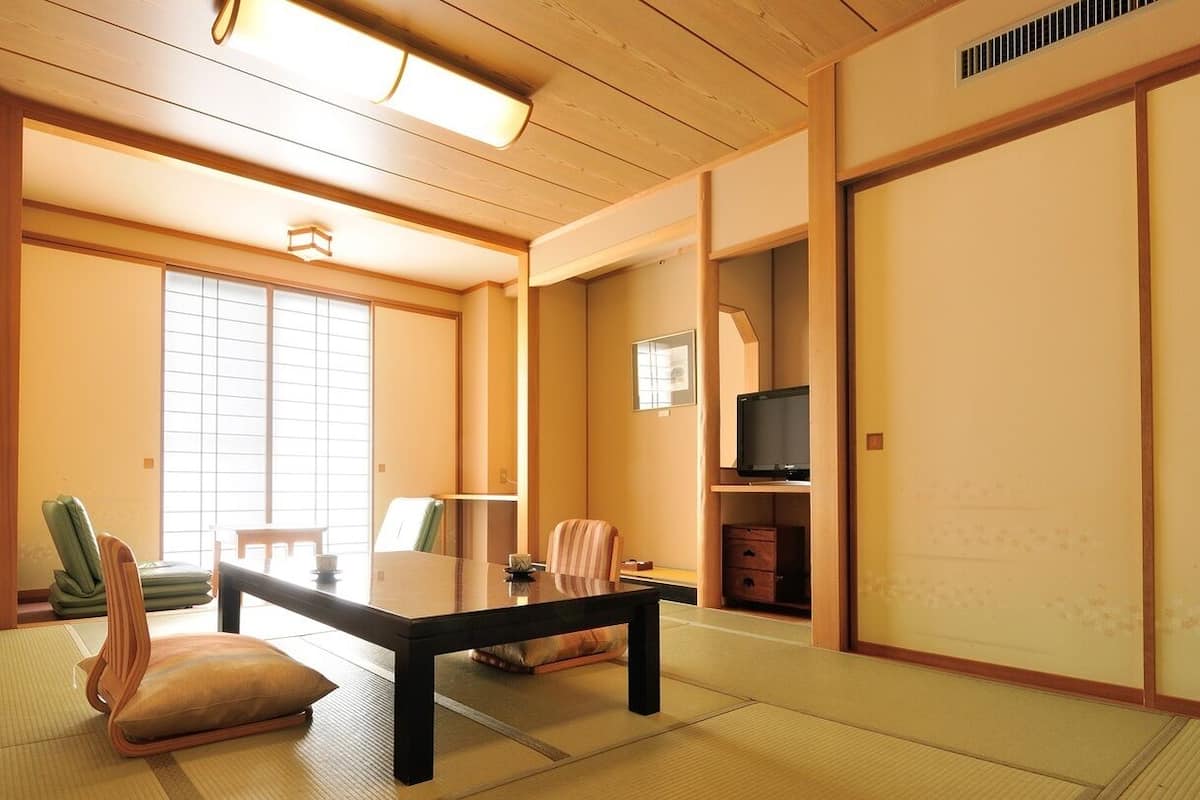 Une pièce de style japonais traditionnel, avec un sol recouvert de tatamis, une table basse, des chaises, un téléviseur et des portes coulissantes.