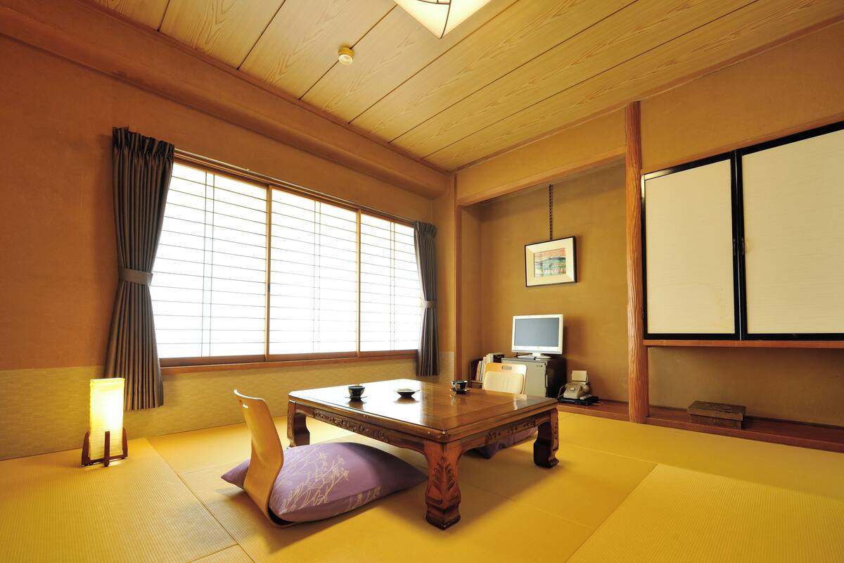 A traditional Japanese room with tatami flooring, a low wooden table, a television, and a shoji screen.