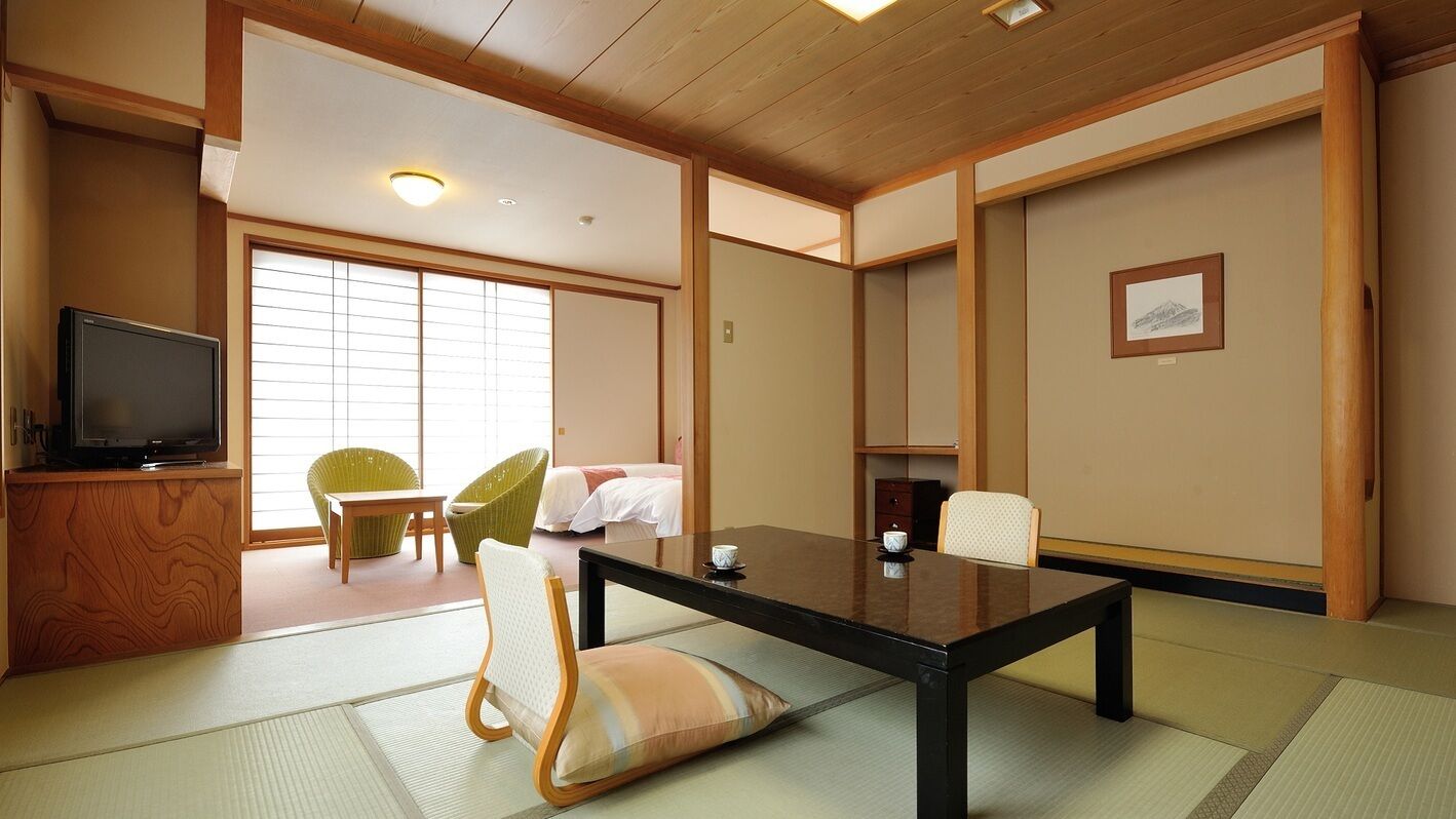 A traditional Japanese-style room with tatami flooring, a low table, chairs, a television, and sliding doors.