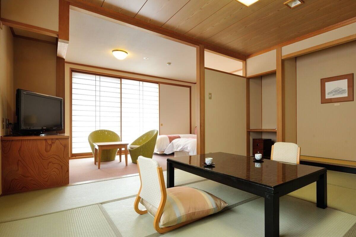 A traditional Japanese-style room with tatami flooring, a low table, chairs, a television, and sliding doors.