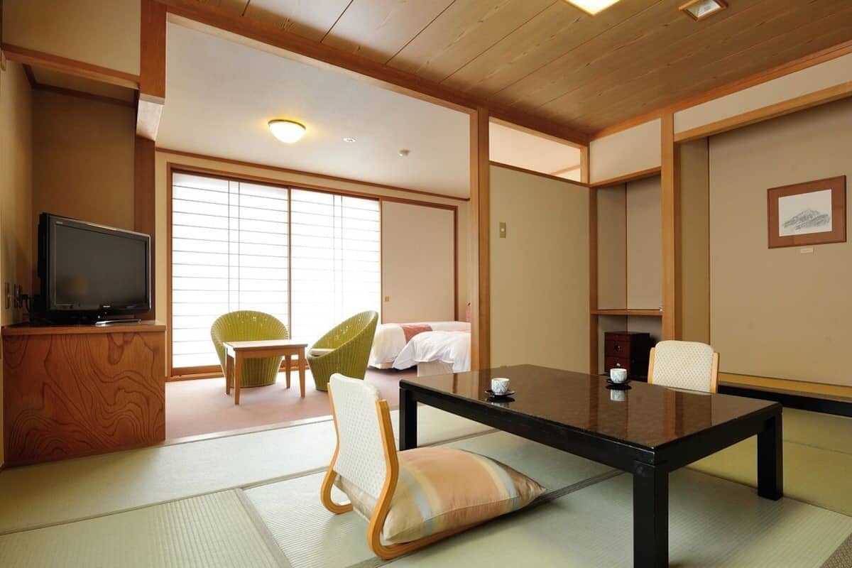 A traditional Japanese-style room with tatami flooring, a low table, chairs, a television, and sliding doors.