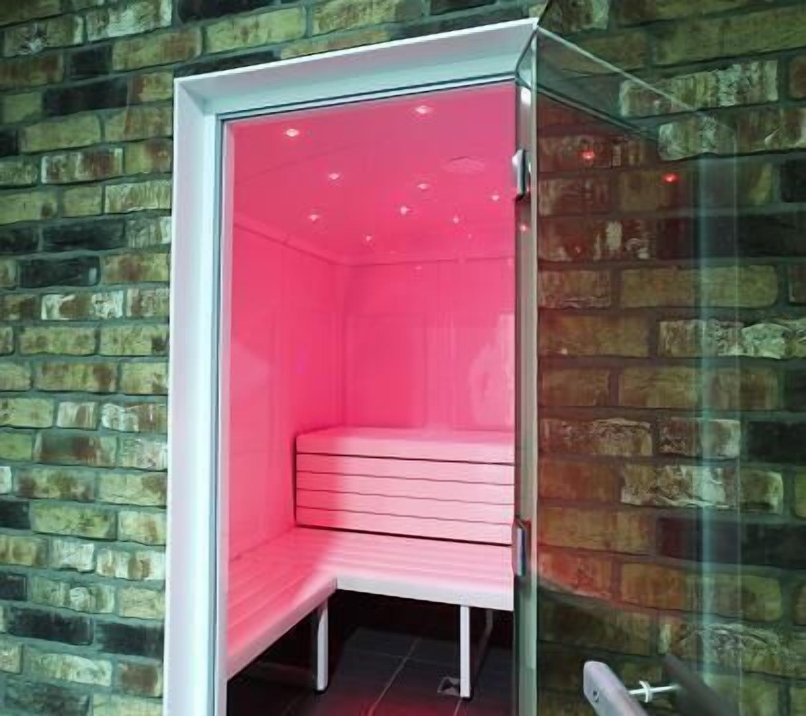 Ein kleiner, abgeschlossener Raum mit rosa Einrichtung und einer Glastür, vor einer Ziegelwand.