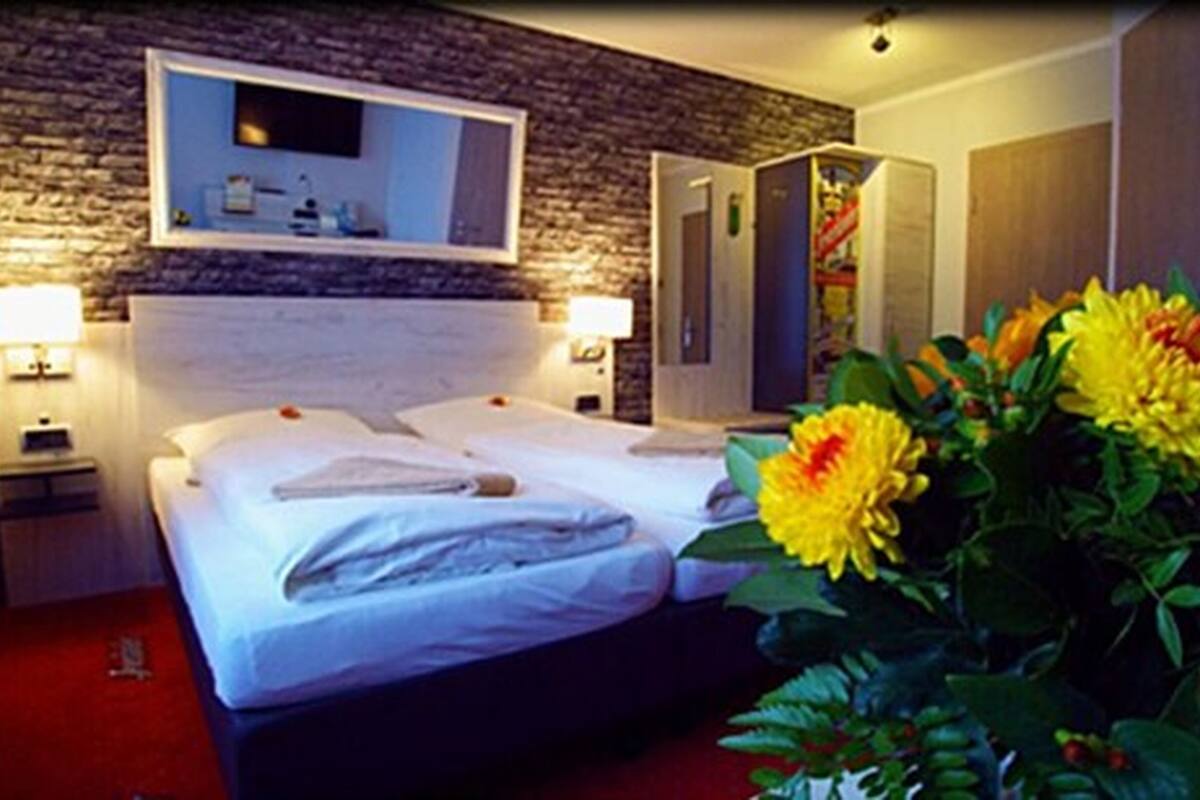 A hotel room with a double bed, two bedside tables, a mirror above the bed, a red carpet, and a large flower arrangement.