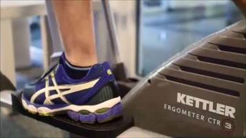 A treadmill with a Kettler ergometer and a person's foot wearing a blue and white athletic shoe.