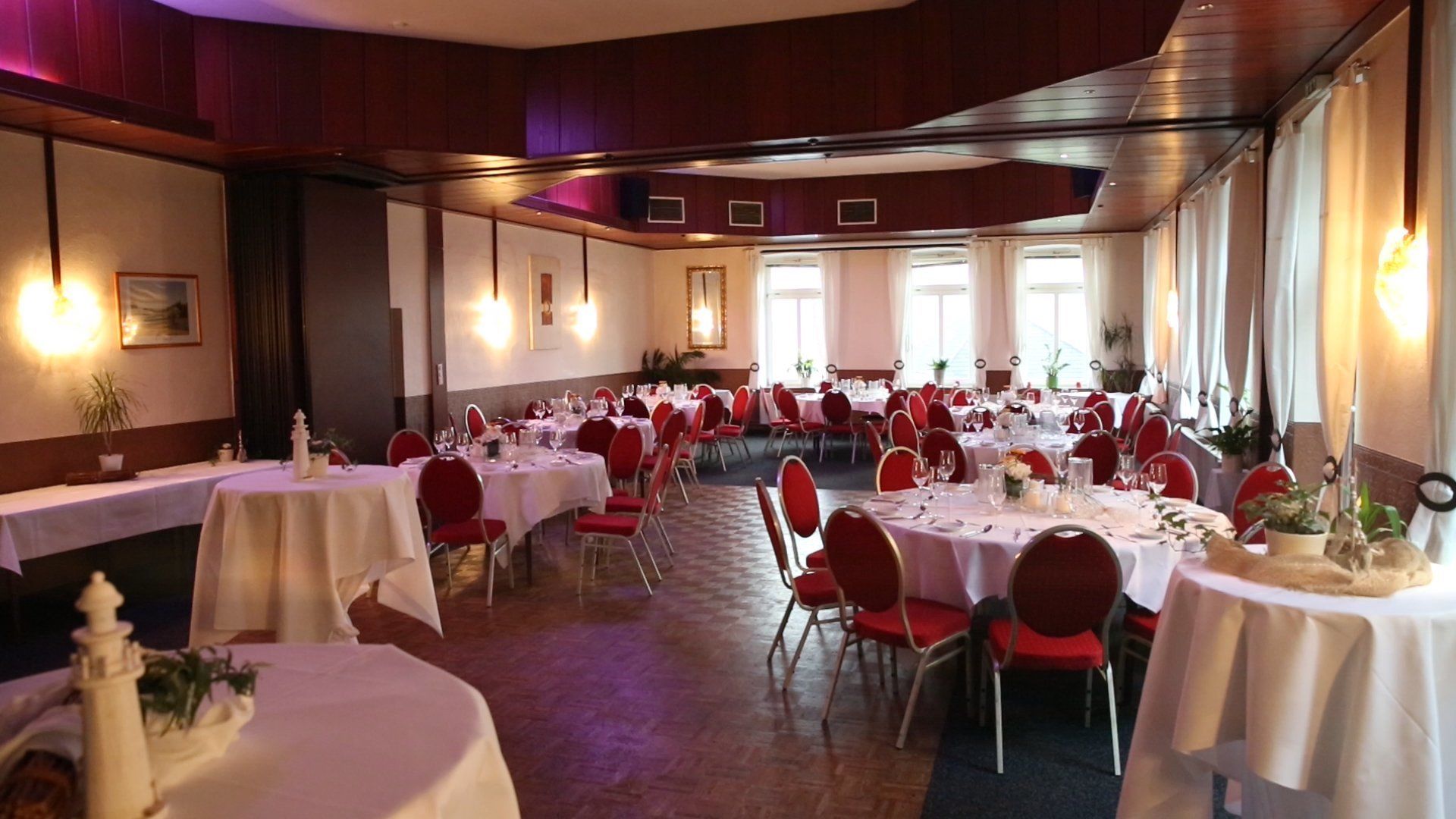 A banquet hall with multiple round tables set for dining, red chairs, and white tablecloths.
