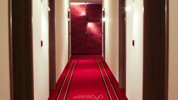 Pasillo de hotel con alfombra roja, puertas de madera y luces fijadas a la pared.