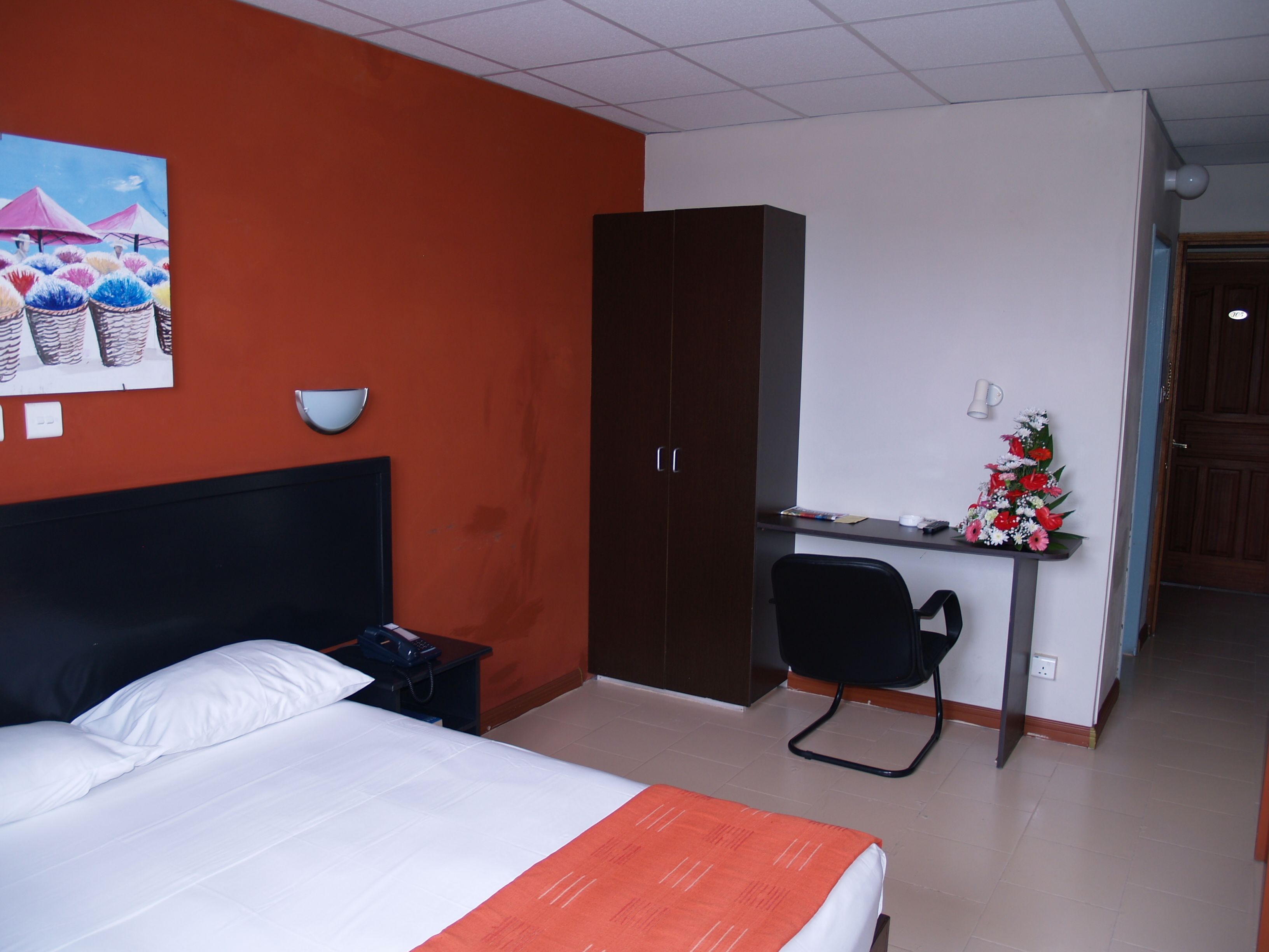 Une chambre d’hôtel avec un lit, un bureau, une chaise, une armoire et un tableau au mur.