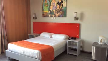 Habitació d'hotel amb un panell de capçal de llit vermell, llit blanc i una manta taronja. Hi ha un quadre a la paret, una tauleta de nit amb una làmpada i un cubell de basures.