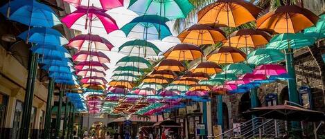 A street with colorful umbrellas overhead, shops, and a staircase.