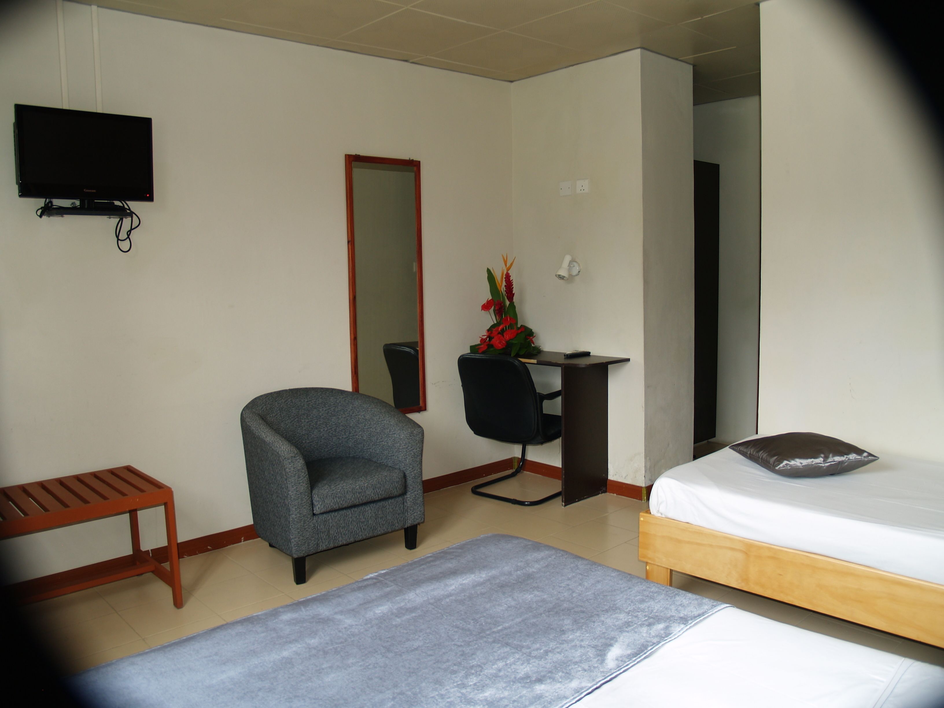 A hotel room with a bed, a desk, a chair, a TV, and a small bench.