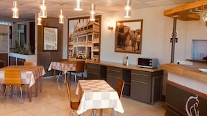 Interior de restaurante com toalhas de mesa xadrez, luminárias pendentes e um balcão com micro-ondas.