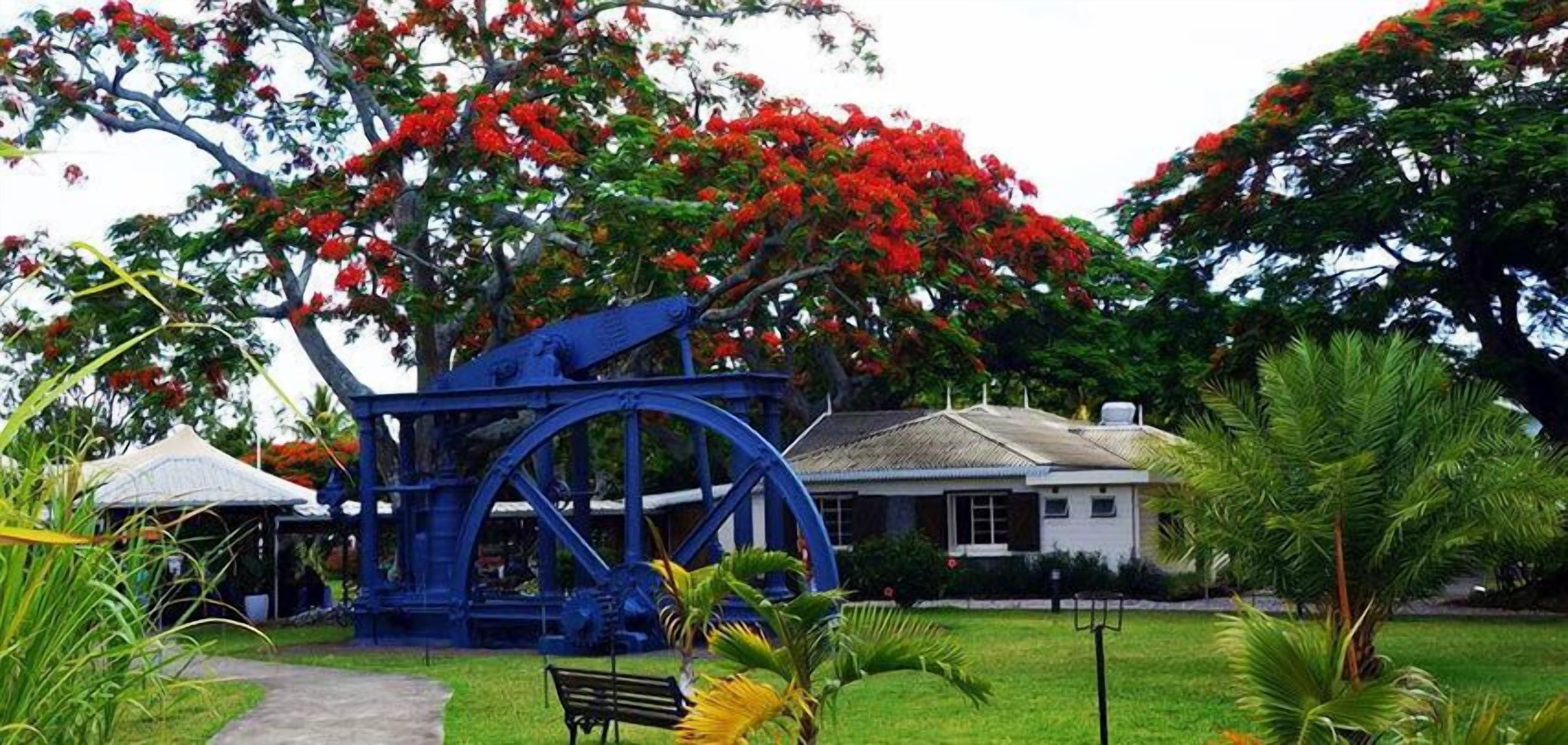 Una estructura de bomba de agua azul en un jardín, con una casa blanca al fondo.