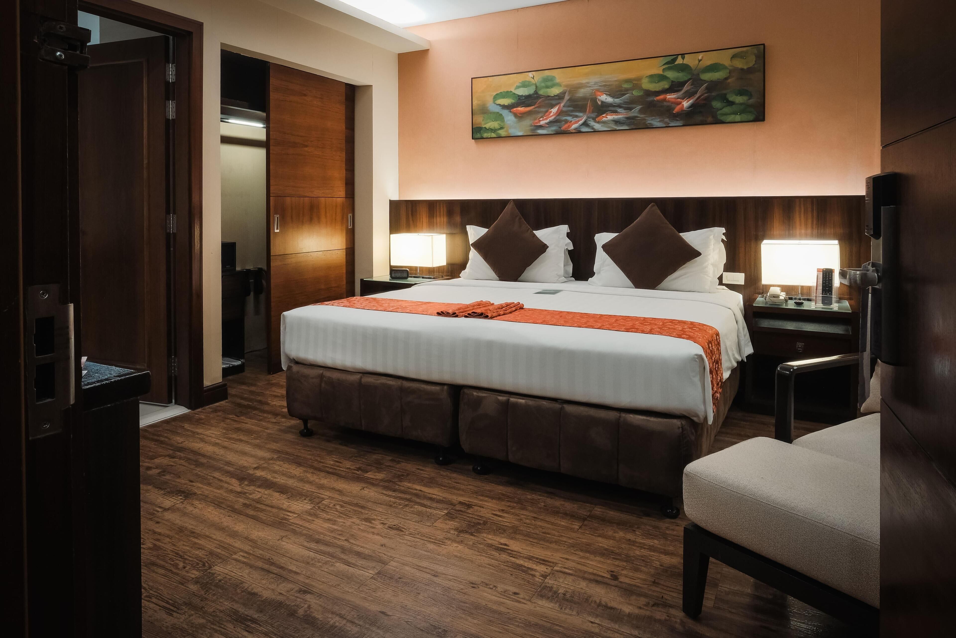 Una habitación de hotel con una cama grande, suelo de madera, un cuadro en la pared y una silla.