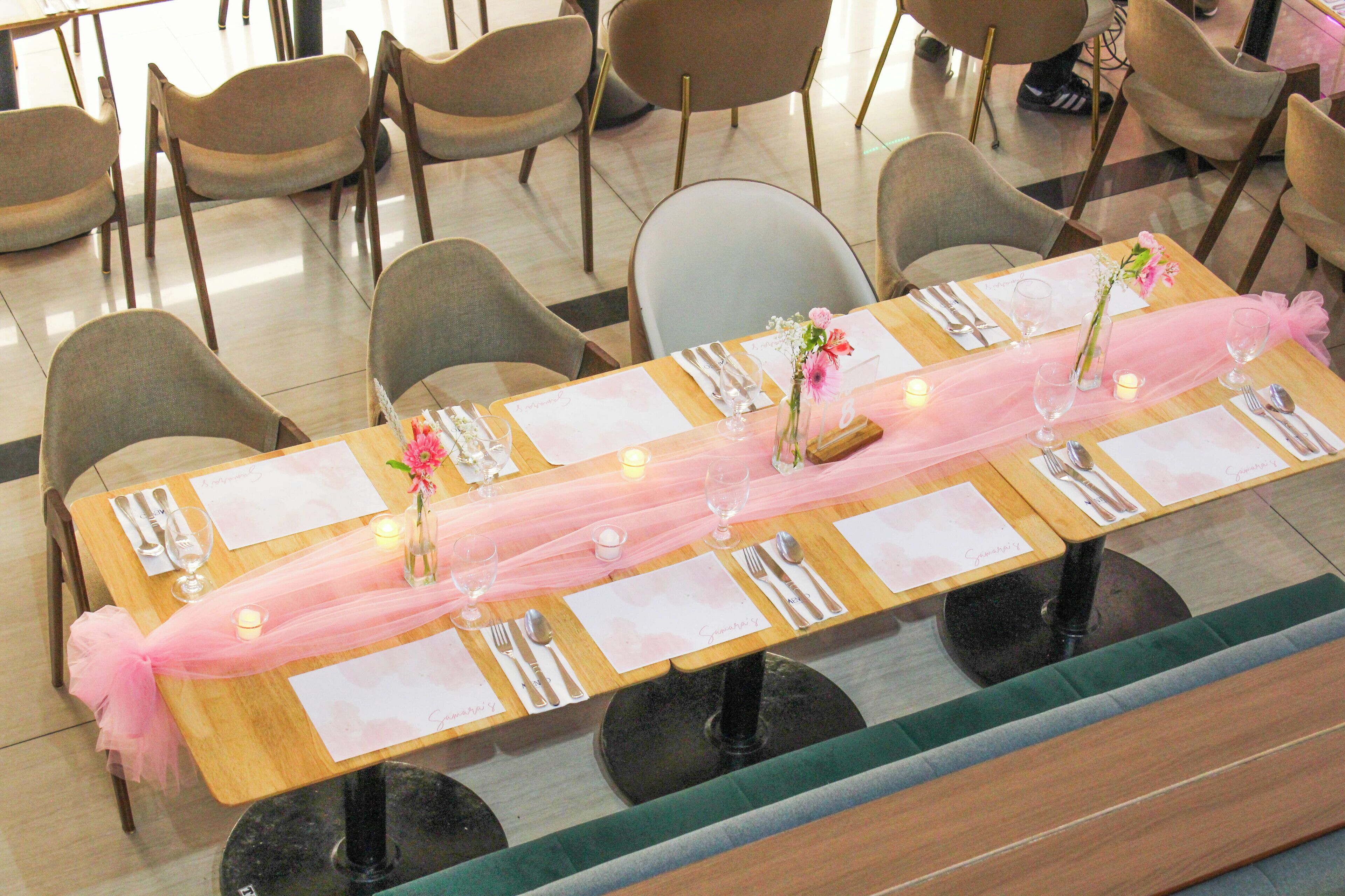 Mesa de comedor decorada con mantel rosa, velas y centros de mesa florales.