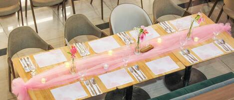 Mesa de comedor decorada con mantel rosa, velas y centros de mesa florales.