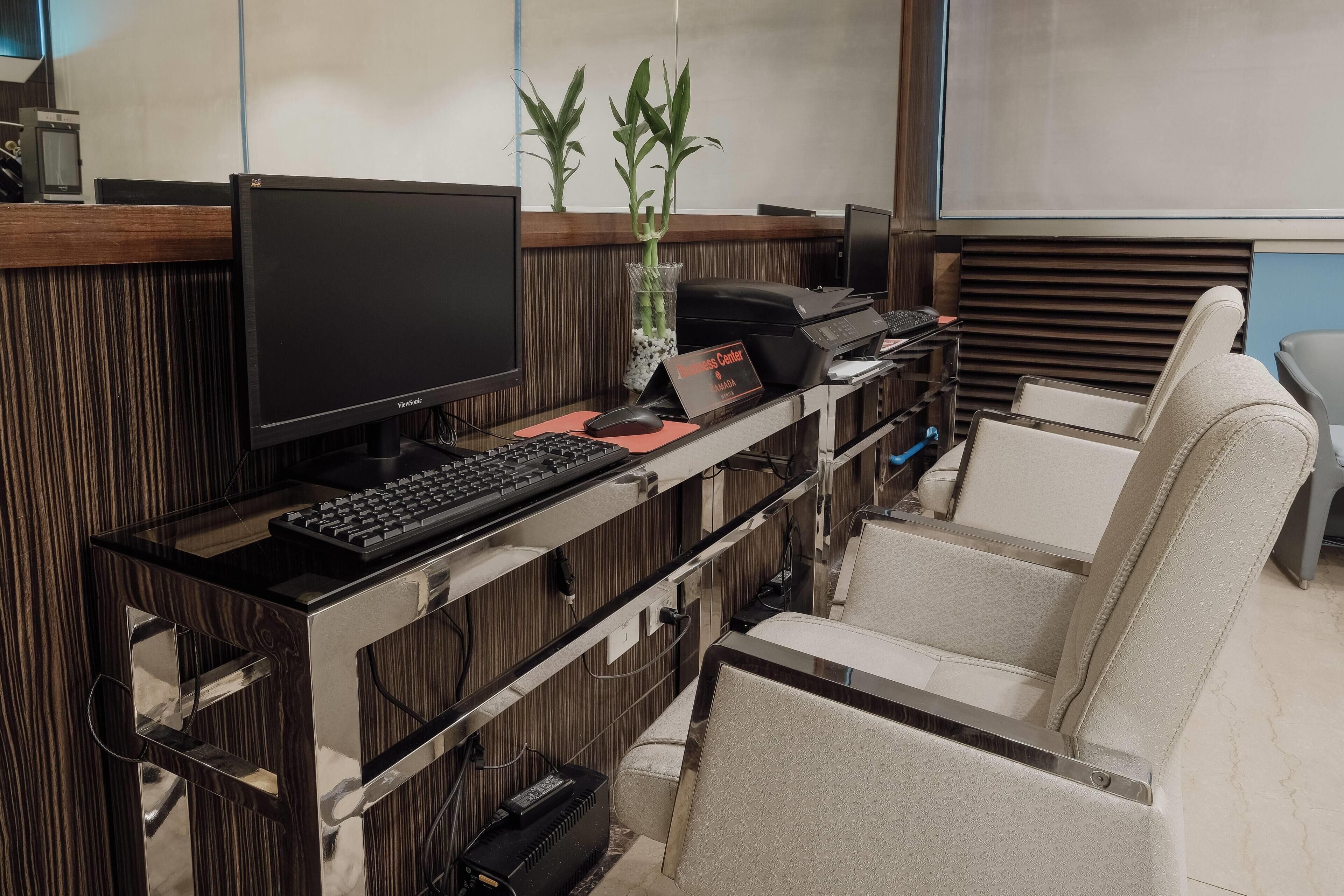 Mostrador de recepción con una computadora, una planta y un letrero que indica la zona central del hotel. Hay sillas y una barra con un teclado.
